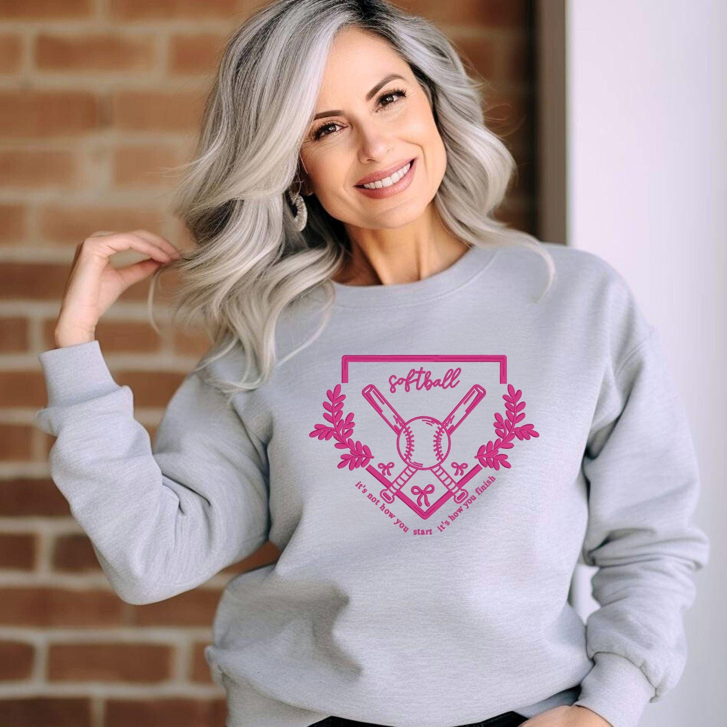 Woman wearing a soft grey embroidered softball sweatshirt, featuring crossed bats and inspirational quote. Perfect for game day style.